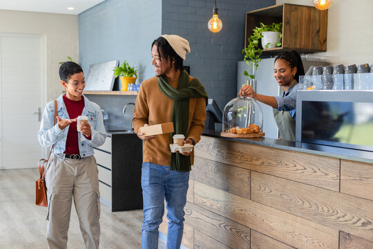 Diverse customers talking while leaving cafe counter holding takeaway cups and cardboard food box