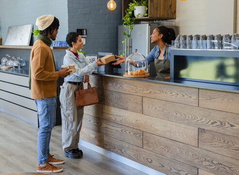 Diverse customers holding takeaway cups pastry box barista serving at coffee bar with QR code sign