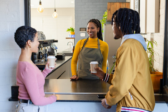 African American barista serving Hispanic woman and African American man cups at espresso machine