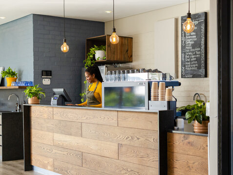 African American barista typing on touchscreen register behind cafe counter near espresso machine