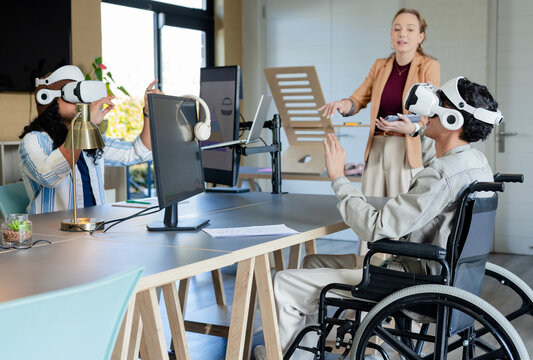 Diverse coworkers demonstrating VR simulation at open plan office with headsets wheelchair monitors