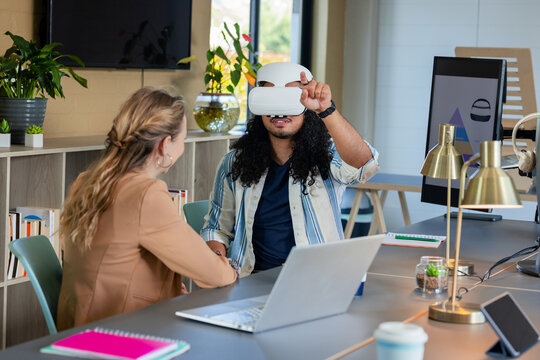 Diverse coworkers collaborating with VR headset and laptop in shared workspace in business attire