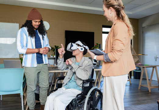 Diverse coworkers demonstrating virtual reality setup in lab with wheelchair, VR headset, tablet