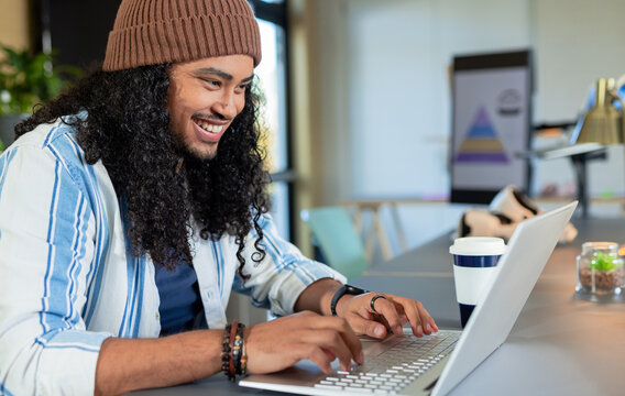 Man wearing knit beanie typing on laptop at office with coffee cup and whiteboard pyramid chart