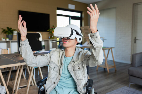 Adult Asian man exploring virtual reality simulation while sitting in wheelchair in home study
