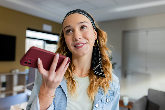 Female office worker holding smartphone recording voice message in office lounge wearing headscarf