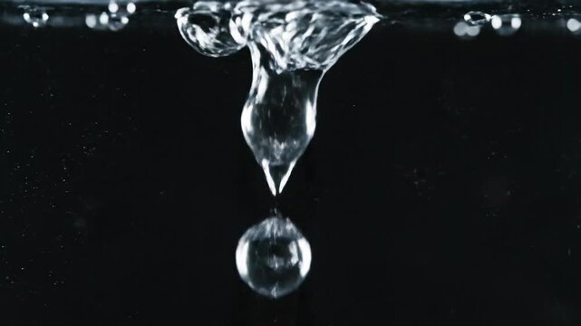 Slow motion water drop forming and falling into clear liquid with bubbles