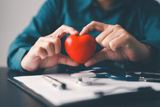 Hands holding red heart above medical documents and stethoscope symbolizing preventive healthcare heart awareness insurance and wellness protection concept