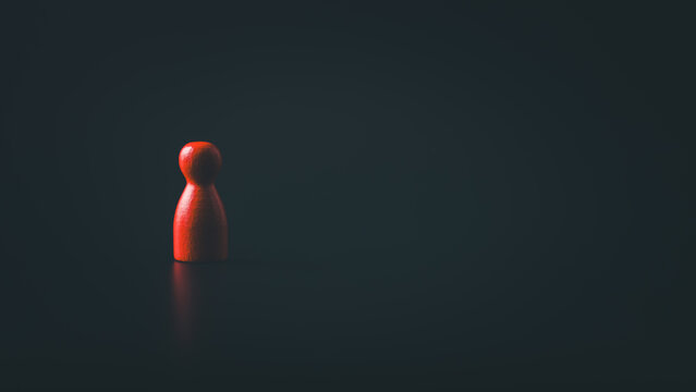 Red wooden figure standing alone in dark background with dramatic lighting symbolizing isolation leadership risk and mental health concept with copy space