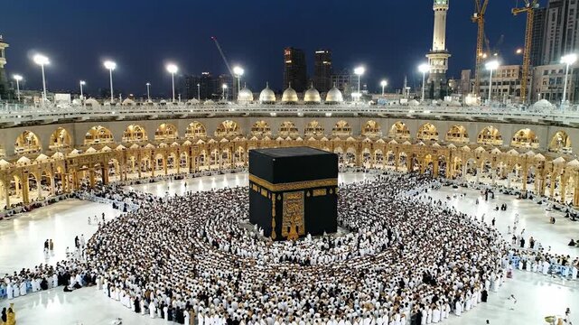 Spiritual journey of millions: Kaaba surrounded by pilgrims performing Tawaf at night, illuminated by the Grand Mosque lights. Ideal for religious documentaries or travel content.