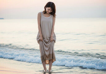 静かな波打ち際でロングワンピースの裾を少し持ち上げ佇む女性