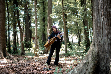 Woman in headscarf playing stringed instrument in sunlit forest