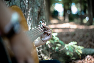 Close-up hands playing acoustic guitar in forest