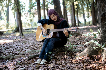 Young woman in hijab playing guitar in forest