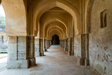 Obraz premium Long view of weathered stone and plaster arcades at Rajon Ki Baoli in Delhi, featuring repeating arches, textured walls, and soft natural light creating a sense of depth and history.