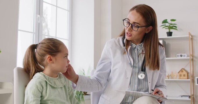 Friendly doctor talking to a child patient. Woman pediatrician in a white coat and glasses giving medical recommendations to a cute little girl. Health care, kids concept