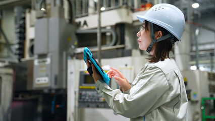 タブレットを持って工場機械を点検する女性作業員