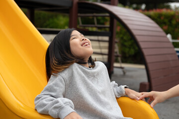 Excited Asian girl sliding quickly down a bright yellow playground slide, shouting with joy and adrenaline © Kwangmoozaa