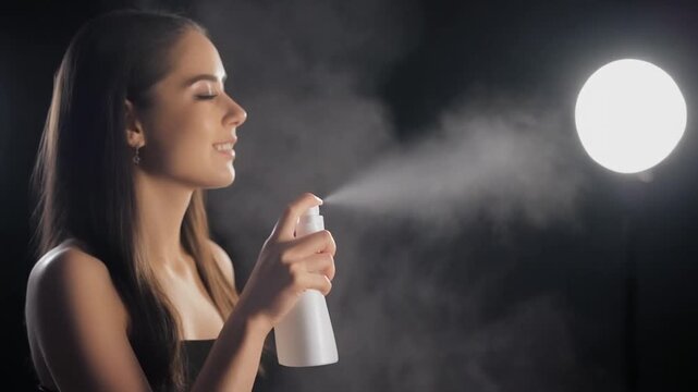 Serene young woman embraces a refreshing beauty ritual, applying a hydrating facial mist for radiant skin with a joyful expression in a luminous setting