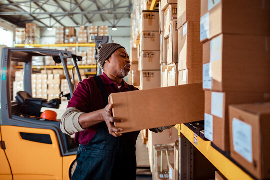 Warehouse worker lifting cardboard box on shelf in distribution center
