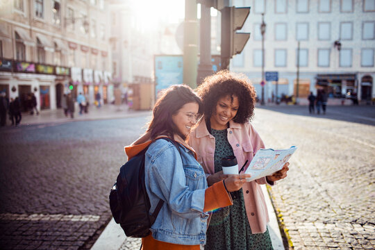 Two friends reading a city map on sunny street