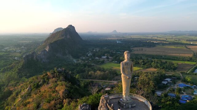 A statue of Jesus standing on a hill in Khao Khup Pha Sawan area, Pak Tho district, Ratchaburi province, Thailand, with houses and factories visible.