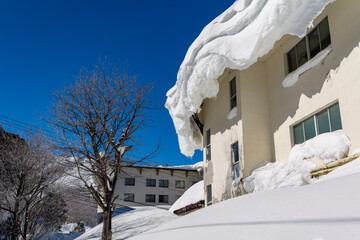 Massive snow cornice hanging off a building roof in Yokoteyama, Shiga Kogen, Japan © whitcomberd