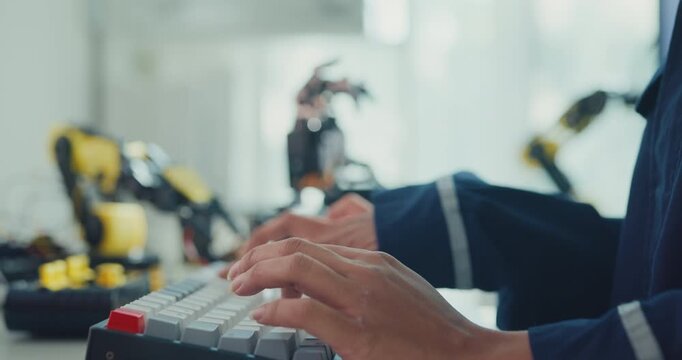Close-up young Black female robotics engineer coding AI software for robotic arm in laboratory. Embedded system, firmware testing, machine learning, industrial automation, future technology concept.