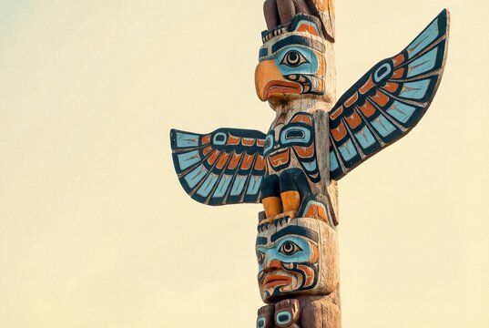 Traditional wooden totem pole with colorful carved eagle and wings against a clear bright sky