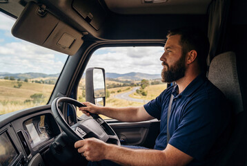 Male truck driver with a beard driving a commercial vehicle on a rural road