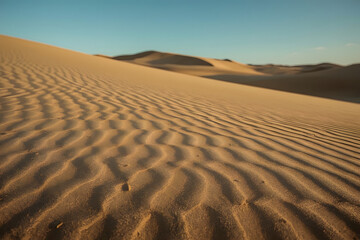 Close-up of rippled sand dunes against a clear blue sky in a desert landscape.