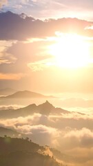 Fototapeta premium Sun shines on a misty mountain range, soft colors of yellow, white, and blue fill the sky