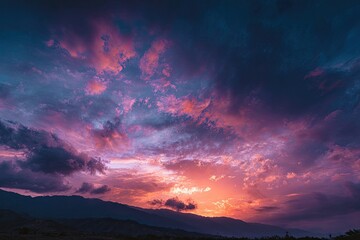 Obraz premium Vivid sunset paints the sky with fiery oranges and pinks above a distant mountain range
