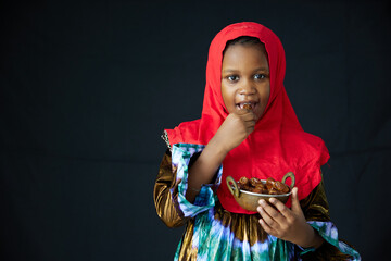 Muslim girl eating dried dates fruits on black background