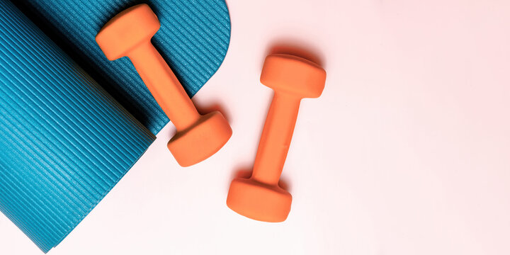 Vibrant orange dumbbells and blue yoga mat on pink, flat lay. Perfect for fitness, exercise, and wellness content. Ample copy space