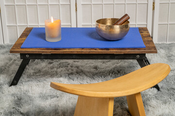 Tibetan singing bowl with a mallet and wax candle on a low table, and kneeling bench, sound healing and meditation concept