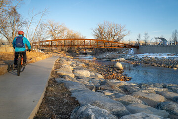 male cyclist is riding a bike in winter sunset scenery - Poudre River Trail in Fort Collins, Colorado at downtown whitewater park, recreation and commuting concept