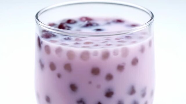 Macro shot of pink bubble tea or dessert drink featuring tapioca pearls (boba) floating in milk in a glass cup on a bright, minimalist background.