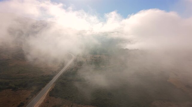 Aerial view of a remote road cutting through dense fog above barren landscape creating mysterious mood cinematic travel scene and sense of isolation.