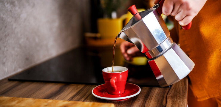 Woman pouring fresh espresso from moka pot into red cup. Strong caffeine drink for morning awakening and productivity.