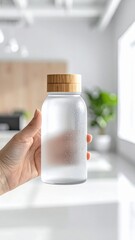 Hand Holding Frosted Glass Bottle With Bamboo Lid Filled With Water And Condensation In Bright Natural Light Room