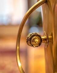 Close Up of Ornate Golden Handle and Decorative Knob on a Polished Metal Vessel with Softly Blurred Warm Background