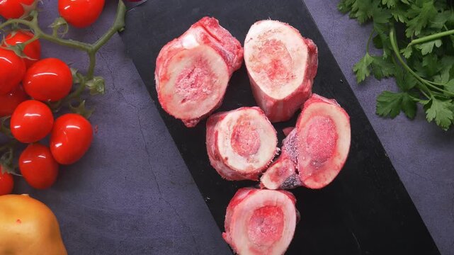 Raw Beef Marrow Bones with Fresh Vegetables on Dark Background