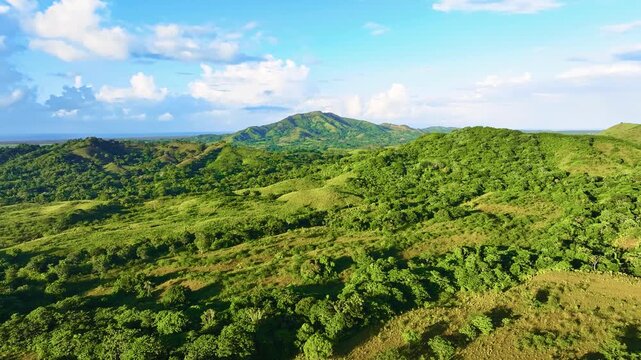Aerial view of a sun-drenched mountain range. Forested foothills under a cloudy sky. Stunning aerial view of a tropical mountain landscape with lush pastures. Dominican Republic.