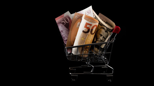 50 euro, 50 US dollar and 50 British pound notes in a miniature supermarket shopping trolley on a black background