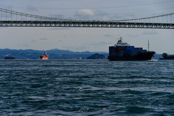 関門橋と関門海峡の波間に進むコンテナ船と満珠干珠20240224-1