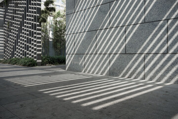 Fototapeta premium Modern architectural facade casting striped light and shadow patterns on stone pavement and wall surface
