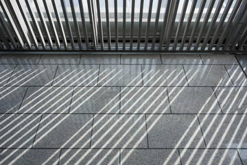 Fototapeta premium Metal railing casts diagonal shadows on gray tiled floor