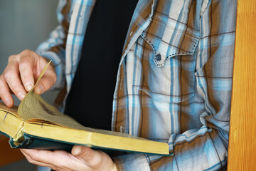 Fototapeta premium Person in Plaid Shirt Reading a Book, Turning Pages Indoors, Casual Attire, Leisure Time, Close-Up