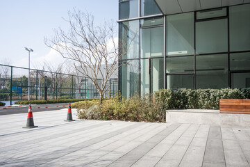 Obraz premium Modern glass building with empty paved plaza and landscaped greenery in daylight